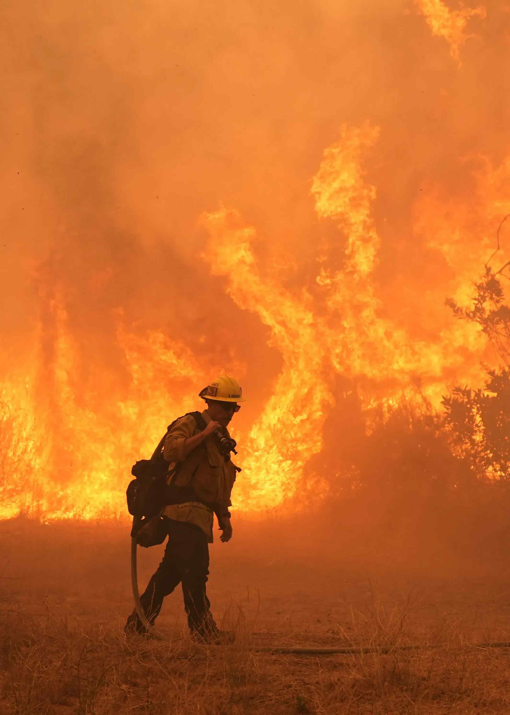 A firefighter with a massive firestorm in the background.